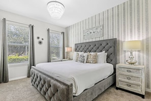 A bedroom with a large bed, a chandelier, striped wallpaper, and a view through the window. - Solara Resort 5BR Home with FlowRider Access (Kissimmee)