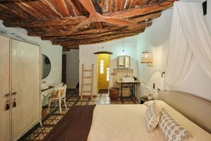 Une chambre à coucher comprenant un lit, un bureau, une chaise, une armoire, un miroir, un lavabo et un ventilateur de plafond.