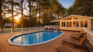 Une piscine dotée d’une terrasse en bois, entourée d’arbres, et un espace couvert avec des sièges.