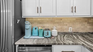 Una cocina con armarios blancos, un refrigerador de acero inoxidable, una cafetera, un tostador y un hervidor.