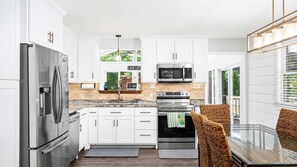A modern kitchen with white cabinets, stainless steel appliances, a microwave, oven, and a dining area with wicker chairs.