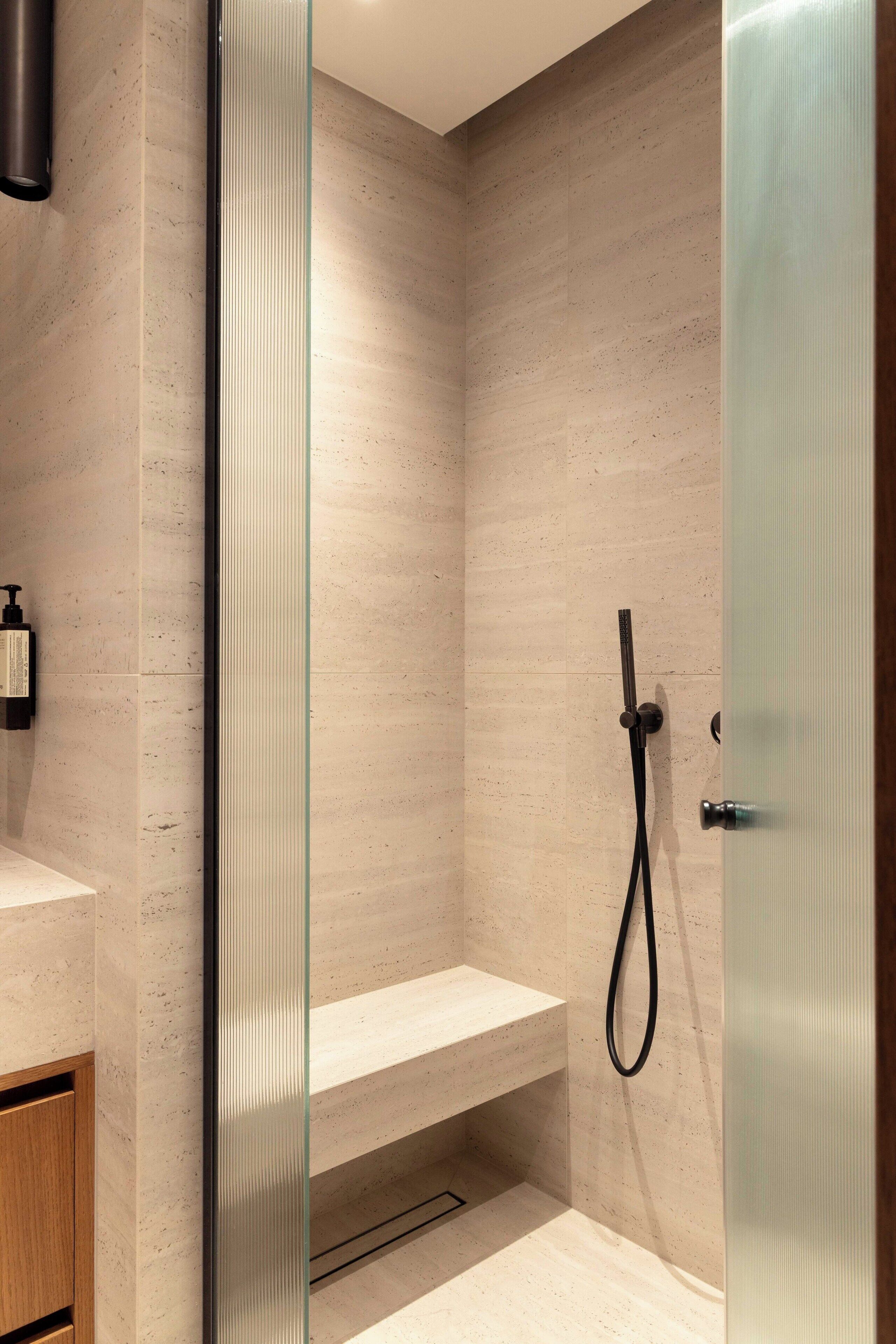 Un baño moderno con cabina de ducha de vidrio, tocador de madera y estante empotrado.