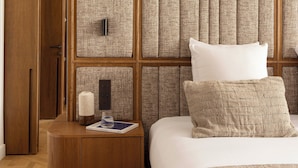Ein Hotelzimmer mit einem Holzschrank, einem Nachttisch mit Lampe, einem Bett mit weißer Bettwäsche und einer Wandverkleidung mit Struktur.
