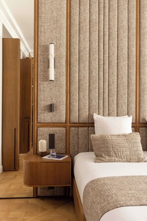 Ein Hotelzimmer mit einem Holzschrank, einem Nachttisch mit Lampe, einem Bett mit weißer Bettwäsche und einer Wandverkleidung mit Struktur.