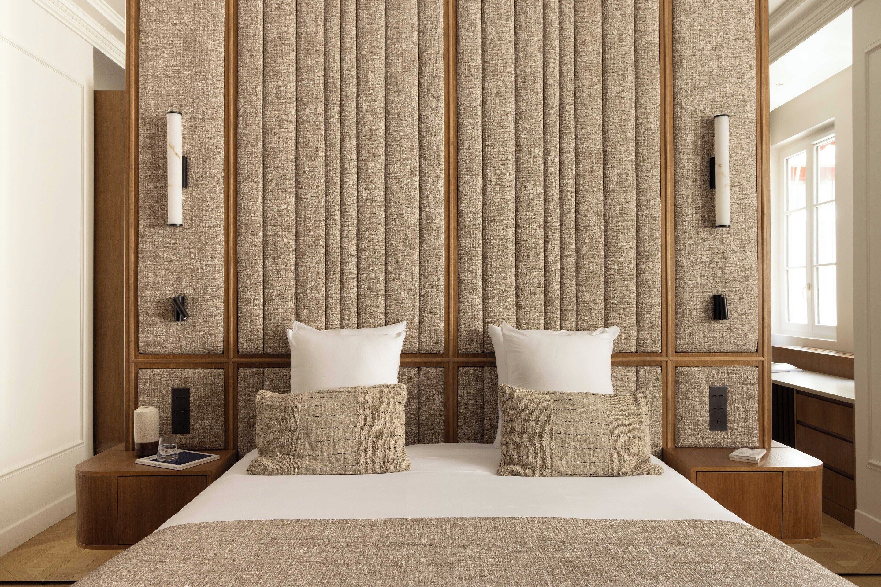 Habitación de hotel con una cama grande, dos mesitas de noche, un diseño de panel en la pared y una ventana.