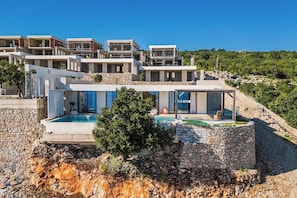 Eine moderne Villa mit Pool, Steinmauern und Blick auf eine Hügellandschaft.