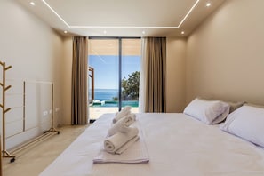 A hotel room with a large bed, a view of the sea, and a sliding glass door leading to an outdoor area.