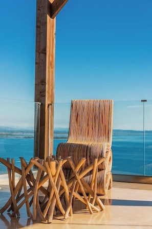Ein Holzhocker mit Streifenmuster, eine Glastrennwand und Blick aufs Meer.