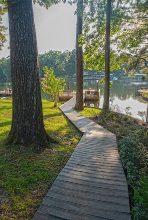 A wooden boardwalk leading to a dock by a lake, surrounded by trees and a small bridge. - Waterfront Home Near Real Island (Eclectic)