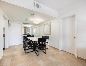 Um quarto amplo com uma grande mesa de jantar, cadeiras e uma cozinha visível ao fundo.