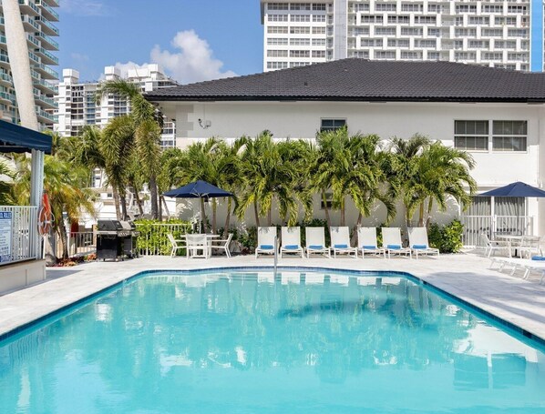 Piscina com espreguiçadeiras e palmeiras, rodeada por edifícios altos.