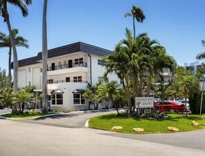 Um edifício com vários andares, fachada branca, palmeiras e uma placa indicando Coconut Bay Resort.