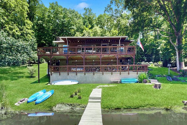 A two-story wooden cabin with a deck, surrounded by a pond and greenery. - Lakeside Cove (Franklin)