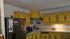 A kitchen with yellow cabinets, a refrigerator, and a tiled backsplash. - Mas de la Cigaline Var (Gareoult)