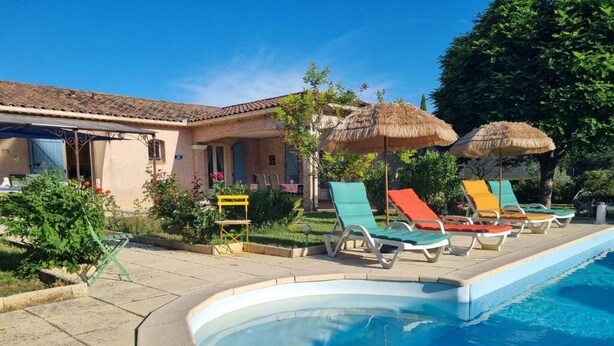 A swimming pool with lounge chairs and umbrellas, a building with a tiled roof, and a clear blue sky. - Mas de la Cigaline Var (Gareoult)