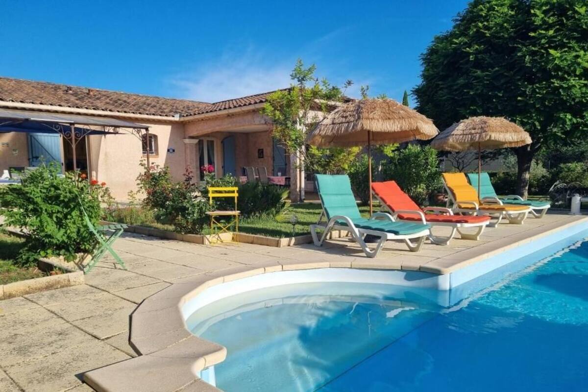 A swimming pool with lounge chairs and umbrellas, a building with a tiled roof, and a clear blue sky.