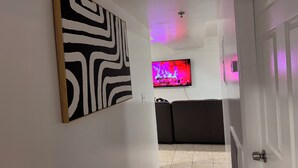 Un passadís amb un quadre abstracte en blanc i negre, un televisor que mostra un foc i un sofà de color fosc.