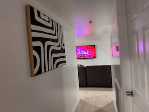 A hallway with a black and white abstract painting, a television displaying a fire, and a dark-colored sofa. - Large 2 Kings bedroom , 2 bathrooms byEWR/NYC Downtown Newark (Newark)