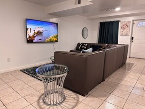 A living room with a flat-screen TV, a glass coffee table, a brown sofa, a round mirror, and a door with a window. - Large 2 Kings bedroom , 2 bathrooms byEWR/NYC Downtown Newark (Newark)
