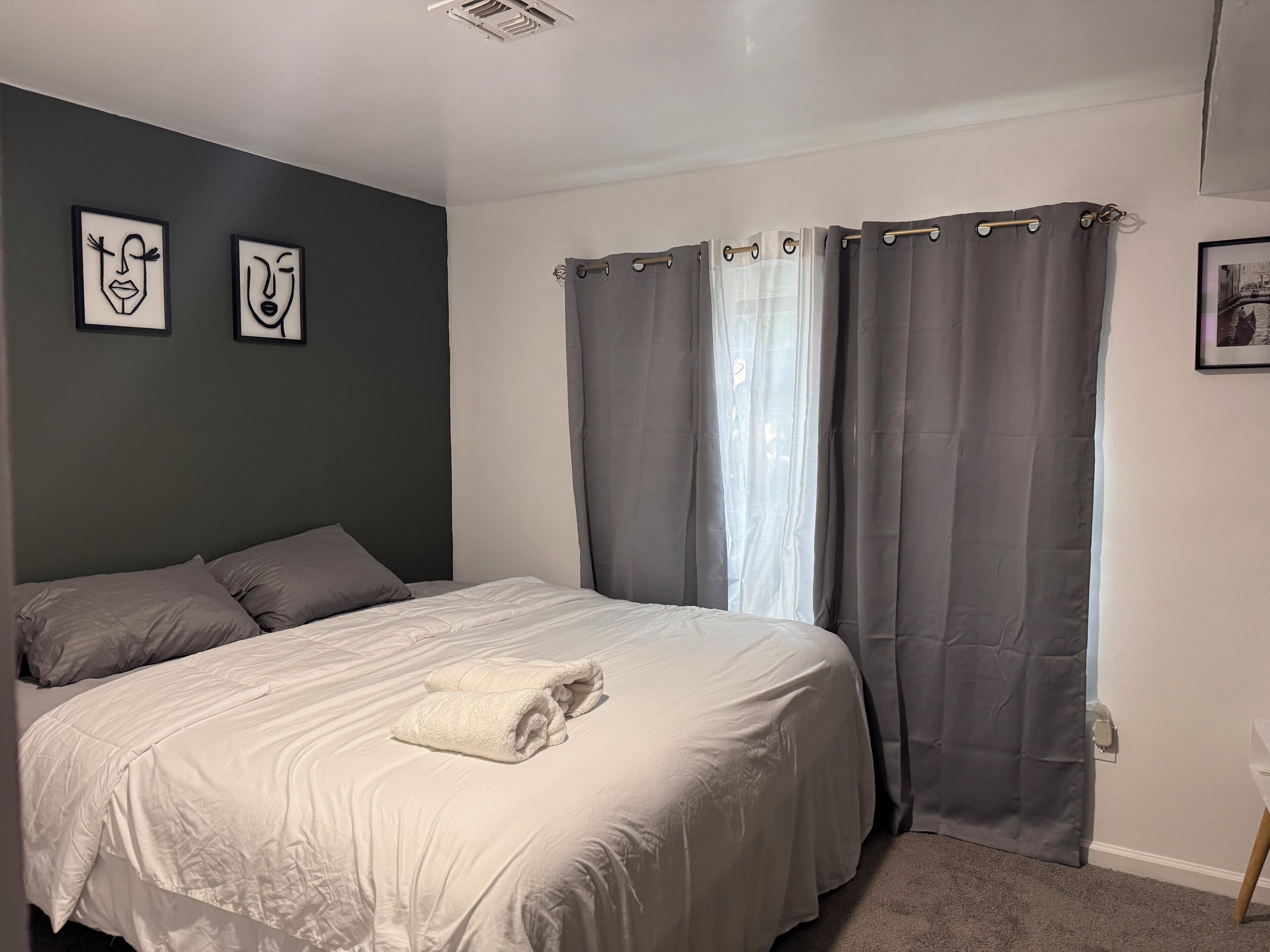 A bedroom with a bed, grey curtains, and two wall art pieces.