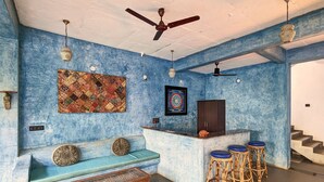 Een kamer met een blauwe, gestructureerde muur, een plafondventilator, een kamerbreed tapijt, een bank, een bar met krukken, en een trap.