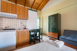 A compact kitchen with wooden cabinets, a white refrigerator, and a dining area with a table and chairs. - Apartment 'Lenia Studio 1' with Mountain View, Wi-Fi and Air Conditioning (Kalamitsi)