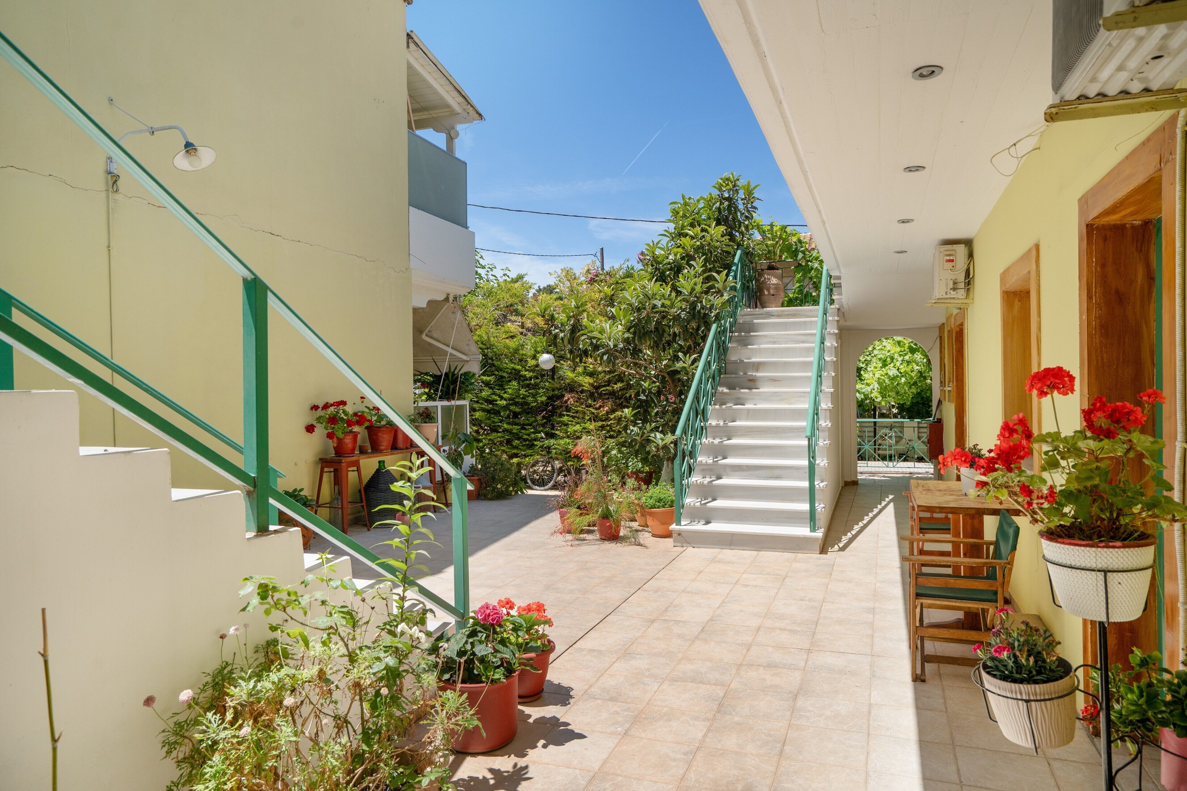 A narrow courtyard with a staircase, potted plants, and a wooden table.