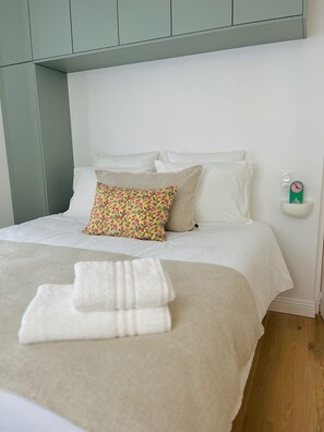 Ein ordentlich bezogenes Bett mit einem blumigen Kissen, einer weißen Decke und einem gefalteten Handtuch.