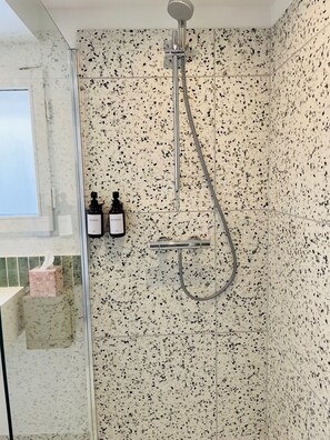 Eine Dusche mit Handbrause und Duschzubehör, ein Fenster sowie zwei Flaschen Shampoo und Conditioner an der Wand.