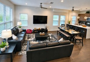 A modern living room with a sofa, coffee table, and TV, a dining area with chairs, and a kitchen with appliances. - Skyline Views | Rooftop Deck | Minutes to Downtown (San Antonio)