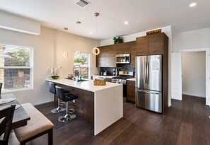 A modern kitchen with a central island, stainless steel appliances, and a dining area with bar stools. - Skyline Views | Rooftop Deck | Minutes to Downtown (San Antonio)