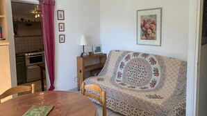 Una sala acogedora con un sofá estampado, una mesa de madera y una cocina visible a través de un vano.