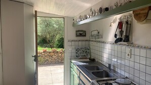 Una cocina con estufa a gas, dos fregaderos, pared de piedra y vistas al exterior.
