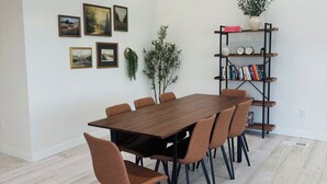 A dining area with a wooden table and chairs, a bookshelf with books and decorative items, and framed pictures on the wall.