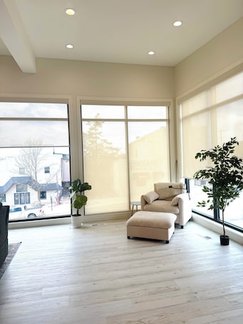 A spacious room with a large sliding glass door, a beige sofa, a small round table, and a potted plant.. NeverHome. Steps to town. Minutes from the lake.