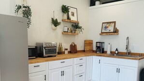 A modern kitchen with white cabinets, a stainless steel refrigerator, a wooden countertop, and a built-in oven.