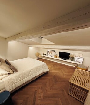 Una camera da letto con un letto, una televisione, uno scaffale con oggetti decorativi e un pavimento in legno.