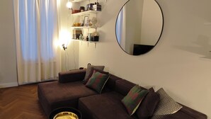 A living room with a sectional sofa, two side tables, a round mirror, and shelves with books and decorative items. - BB Suite Florence – Elegance, Comfort, Hospitality. (Firenze)