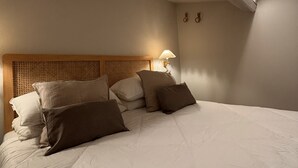A bedroom with a wooden headboard, a bed with white bedding, a bedside lamp, and a sloped ceiling. - BB Suite Florence – Elegance, Comfort, Hospitality. (Firenze)