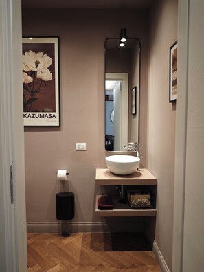 Un bagno moderno con un lavandino bianco, uno specchio, un quadro incorniciato con fiori e un porta carta igienica.