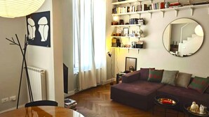 A living room with a round wooden dining table, a sofa, a mirror, and a bookshelf. - BB Suite Florence – Elegance, Comfort, Hospitality. (Firenze)