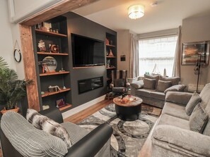 A living room with a sofa, armchairs, a coffee table, a TV, and shelves with various items. - Memory Maker (Bridlington)