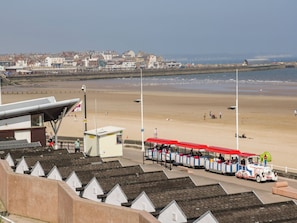 Uma estação de trem à beira-mar com vista para a costa, uma praia de areia e uma fileira de casas brancas ao fundo.