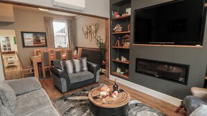A modern living room with a sofa, armchair, coffee table, and a flat-screen TV mounted on the wall. - Memory Maker (Bridlington)