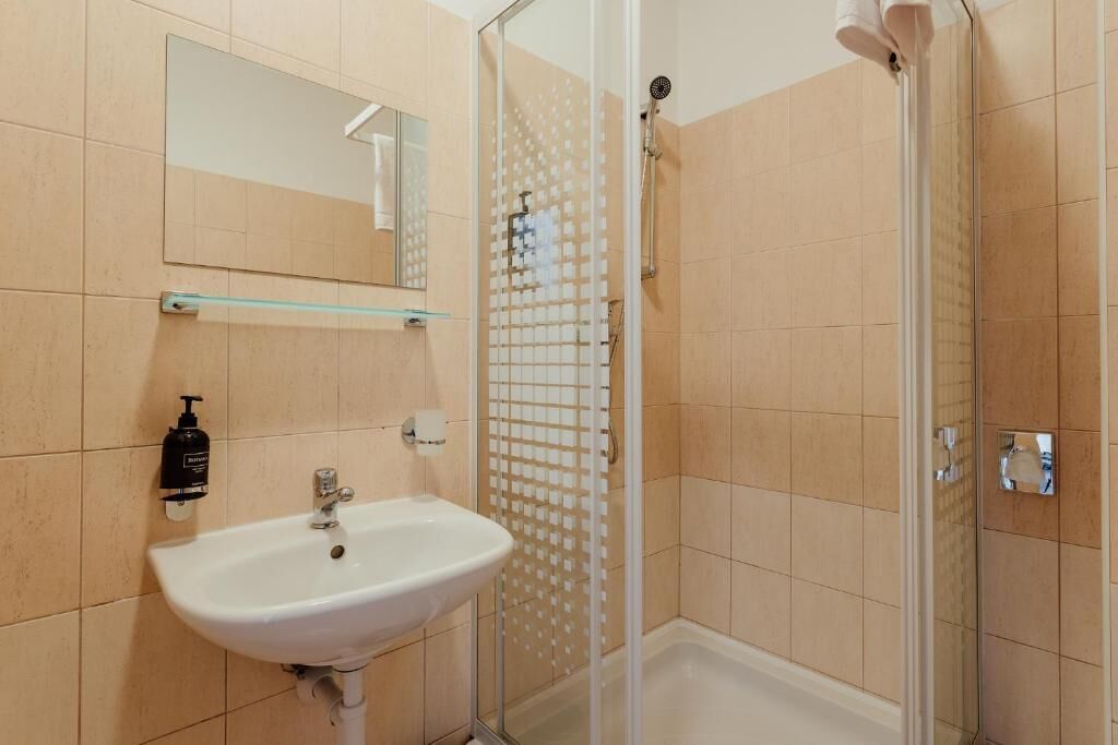 A bathroom with a sink, mirror, and shower enclosure.