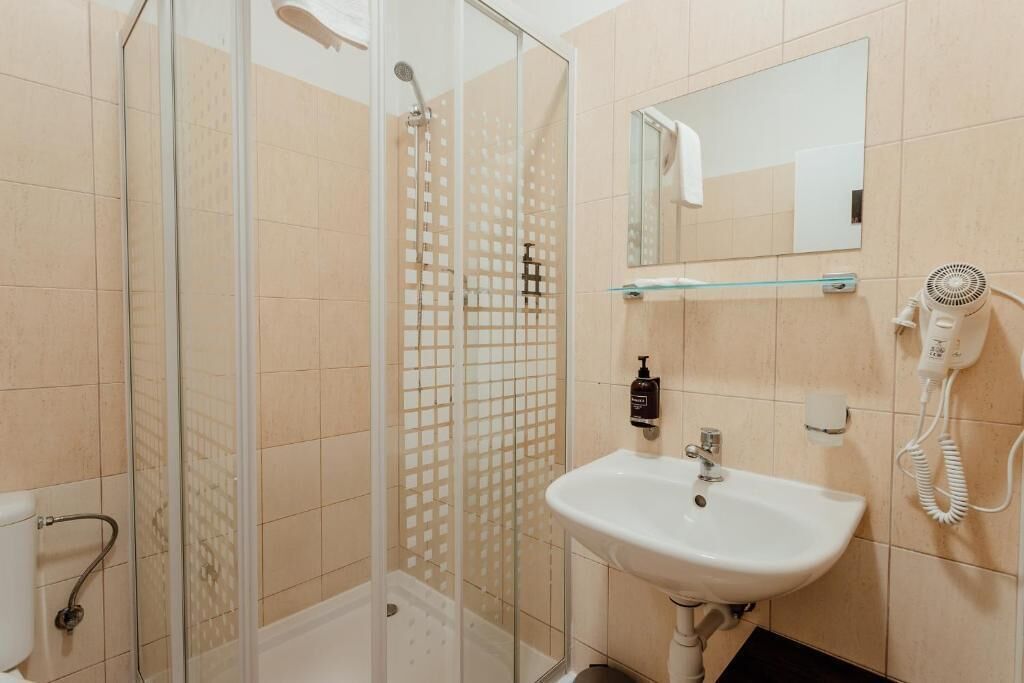 Un baño con cabina de ducha de vidrio, lavamanos blanco, espejo y secador de pelo.