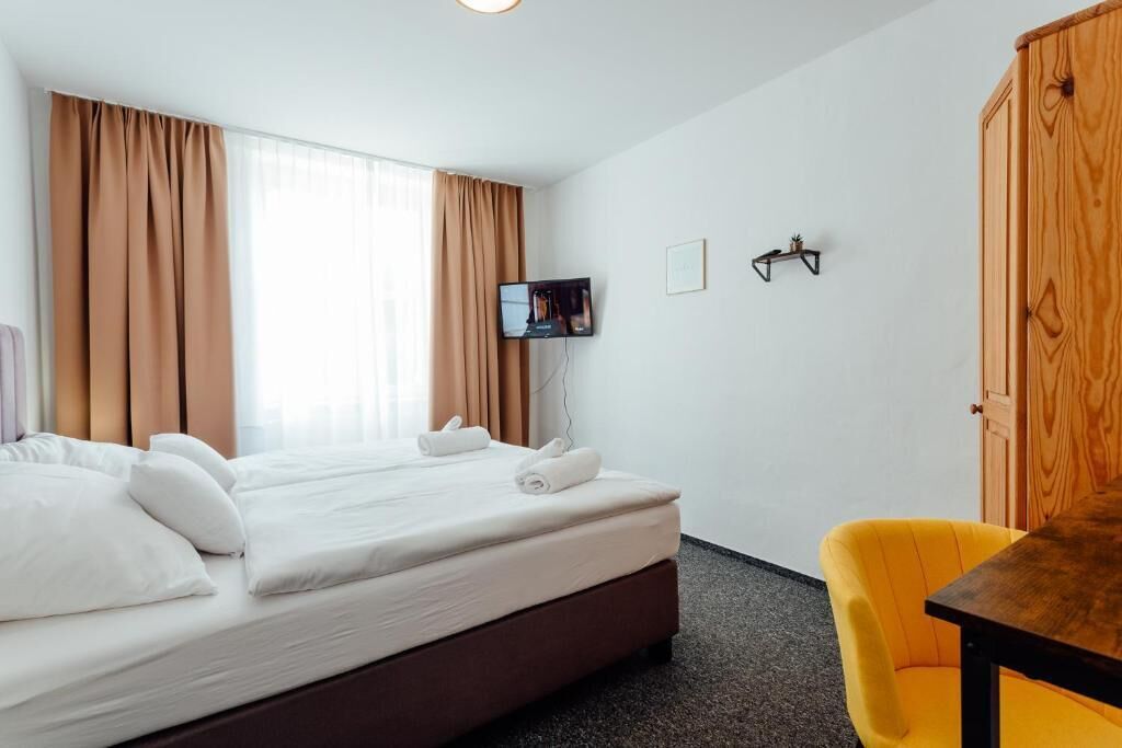 Una habitación de hotel con una cama, televisión, armario de madera y una silla amarilla.