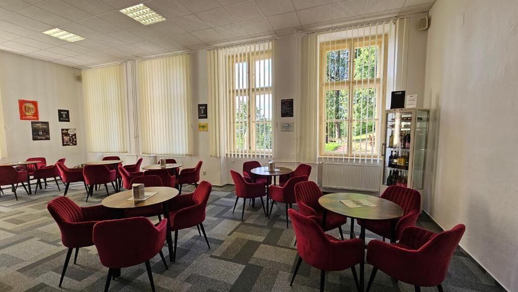 A conference room with red chairs and tables, large windows with blinds, and a radiator.