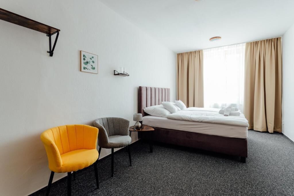 A hotel room with a bed, a chair, a bedside table, and a window with curtains.