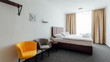 A hotel room with a bed, a chair, a bedside table, and a window with curtains.
